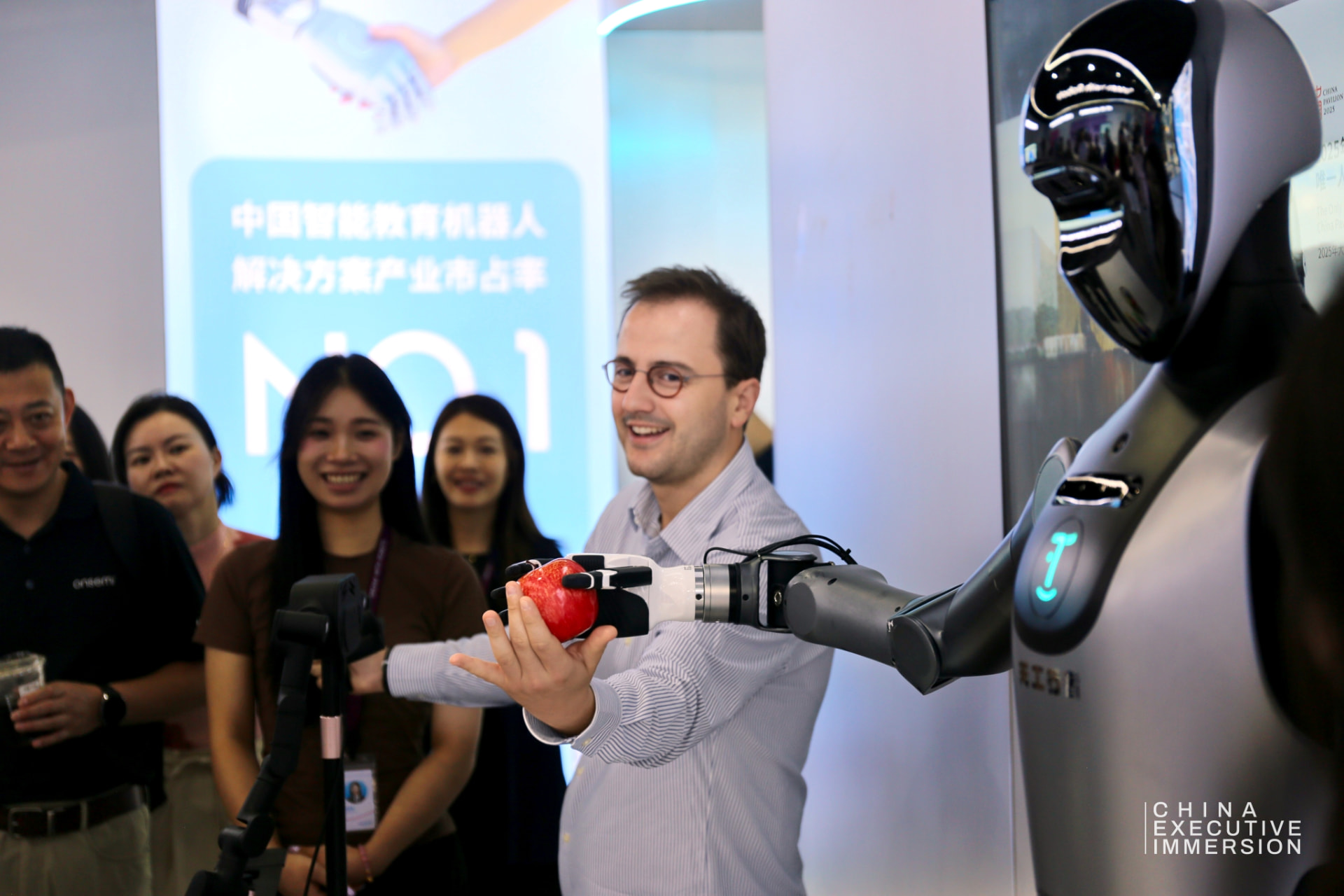 UBTECH — a delegate taking an apple from the hand of an industrial humanoid — Shenzhen 2026